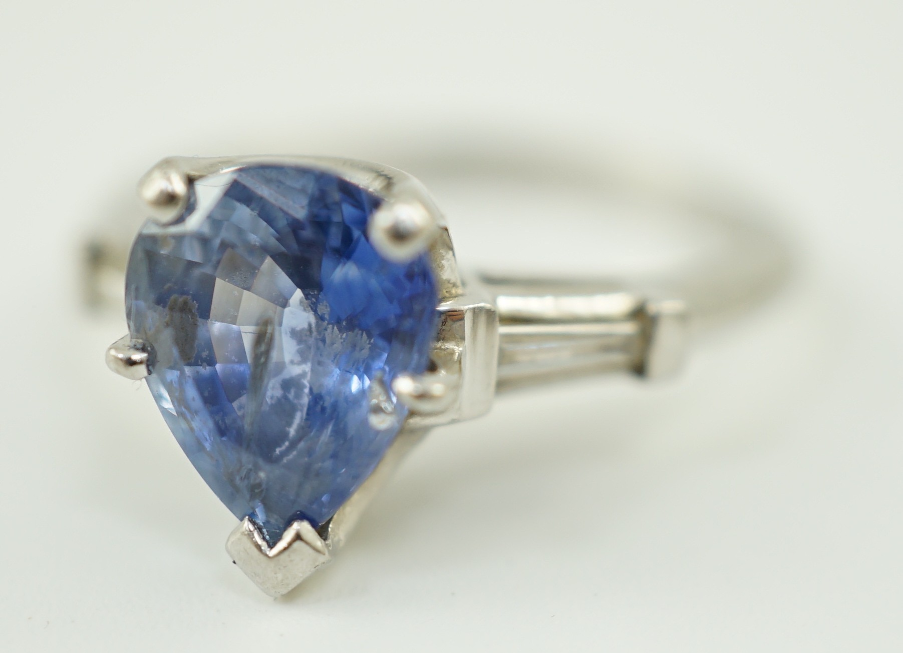 A platinum (10%) and single stone pear cut Ceylon sapphire set ring, with tapered baguette cut diamond set shoulders